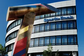 A modern office building with the sign “Sparda-Bank” on the facade. In front of the building stands a large, colorful abstract hammer sculpture against a bright blue sky.