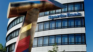 A modern office building with the sign “Sparda-Bank” on the facade. In front of the building stands a large, colorful abstract hammer sculpture against a bright blue sky.