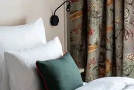 Cozy bed with white linens, green accent pillow, floral curtains, and a modern black wall lamp.