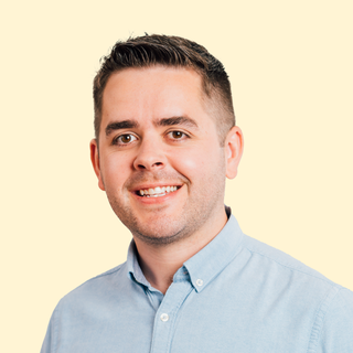 Smiling man in a light blue shirt against a plain cream background.