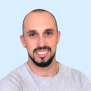A smiling man with a goatee, wearing a gray shirt, against a solid light blue background.