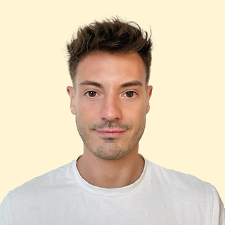 A man with short, styled hair and a slight smile, wearing a white shirt, against a pale yellow background.
