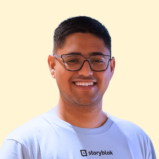 Smiling man wearing glasses and a Storyblok T-shirt against a light beige background.