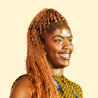 Smiling person with orange braided hair wearing a patterned top and headset, speaking confidently against a light background.