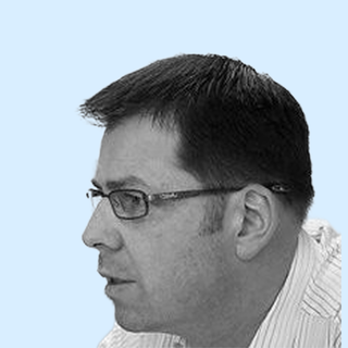 Profile of a man with short dark hair and glasses, seen in black and white against a light blue background.