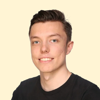 Smiling person with short dark hair, wearing a black shirt against a light background.
