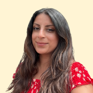 Woman with long hair in a red, floral dress smiles against a beige background.