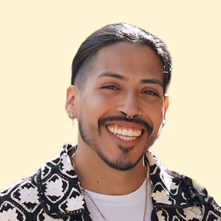 Smiling person with a patterned shirt and nose ring, hair pulled back, against a light background.