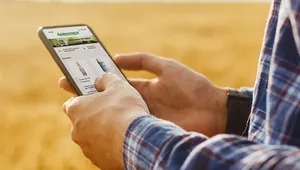 Person using a smartphone with an agricultural app in a wheat field, wearing a plaid shirt.