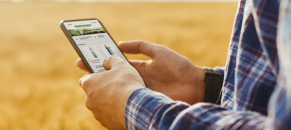 Person using a smartphone with an agricultural app in a wheat field, wearing a plaid shirt.