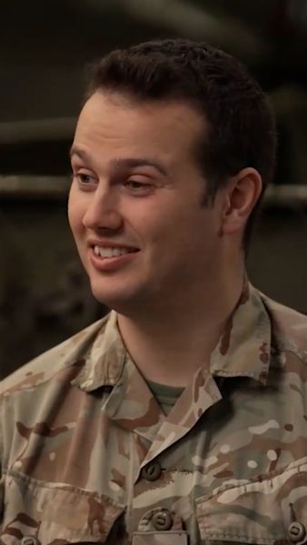 A person in a military camouflage uniform is smiling and looking to the side.
