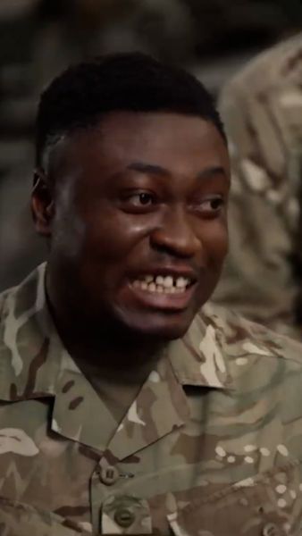 A person in a camouflage military uniform smiling broadly.