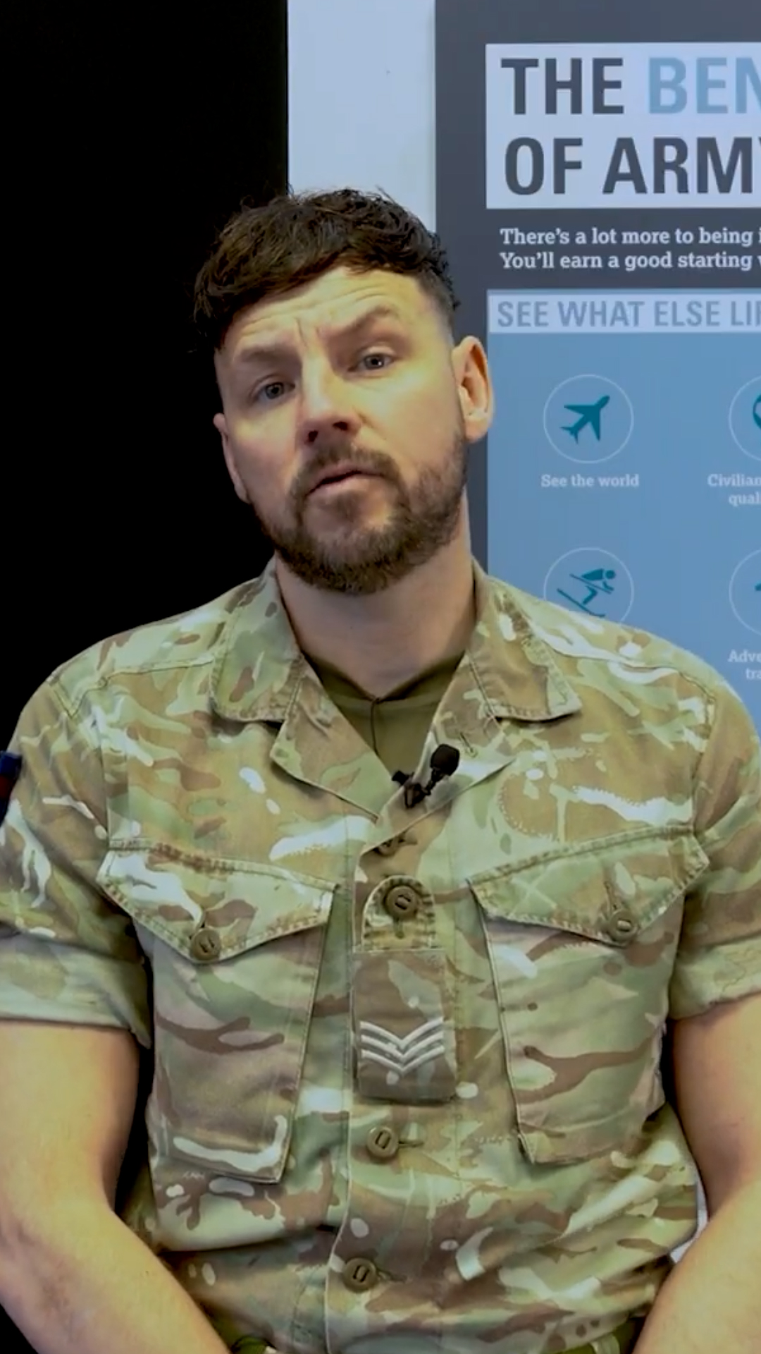 A man in a camouflage military uniform is sitting in front of a blue poster displaying information about the benefits of joining the army.