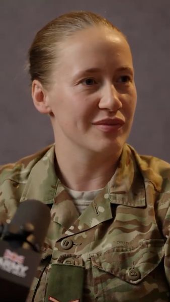 Person in military uniform with a calm expression, seated in front of a microphone.