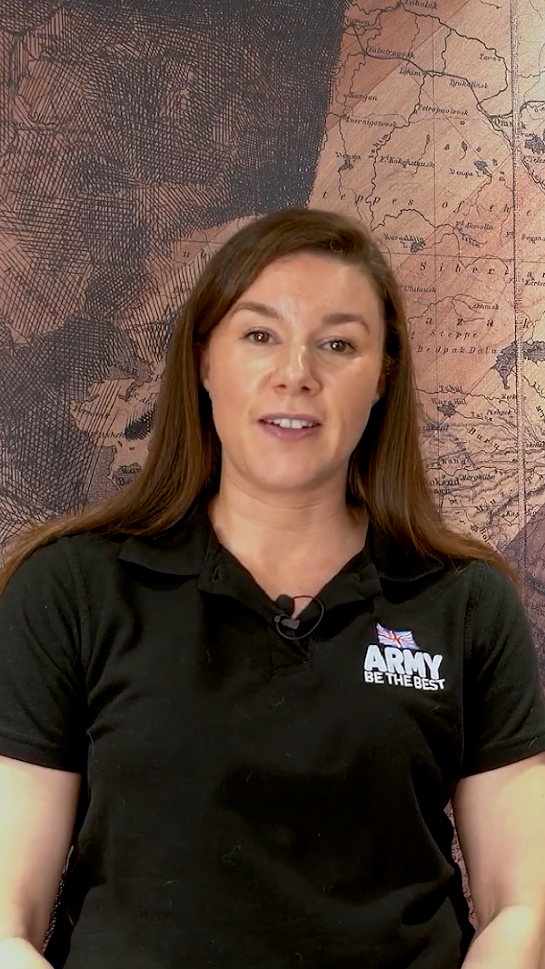 Woman in a black shirt with "Army Be The Best" logo, standing in front of a vintage map background, smiling at the camera.