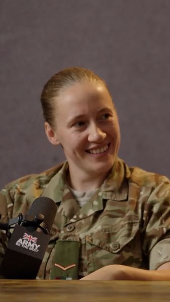 A person in military uniform smiles while seated at a table with a microphone labeled "Army" in front of them.