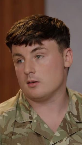 A person in a camouflage military uniform looking off to the side, with a neutral expression.