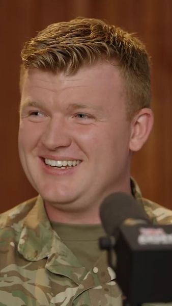A smiling person in a military uniform speaks into a microphone.