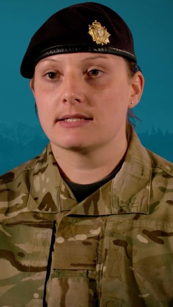 A person in military uniform with a black beret featuring an insignia, standing in front of a blue background.