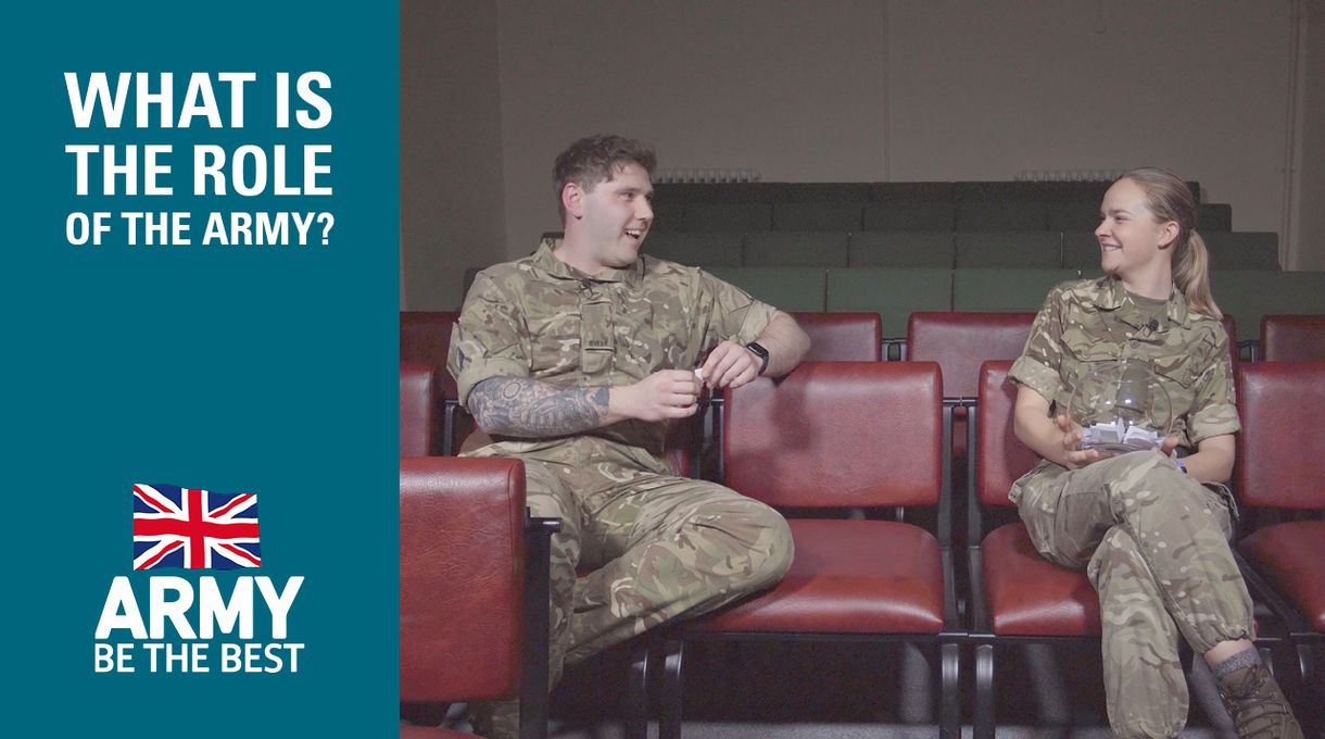 Two soldiers in uniform sit and chat in a lecture hall. Text reads, "What is the role of the Army? Army Be The Best" with a UK flag.