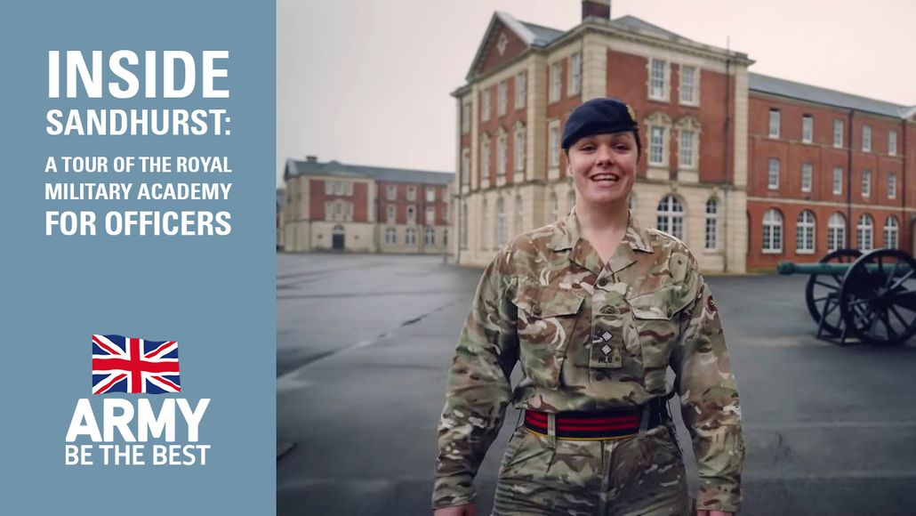 A female officer in military uniform stands smiling in front of a historic building at Sandhurst, with the slogan "Army Be the Best" beside her.