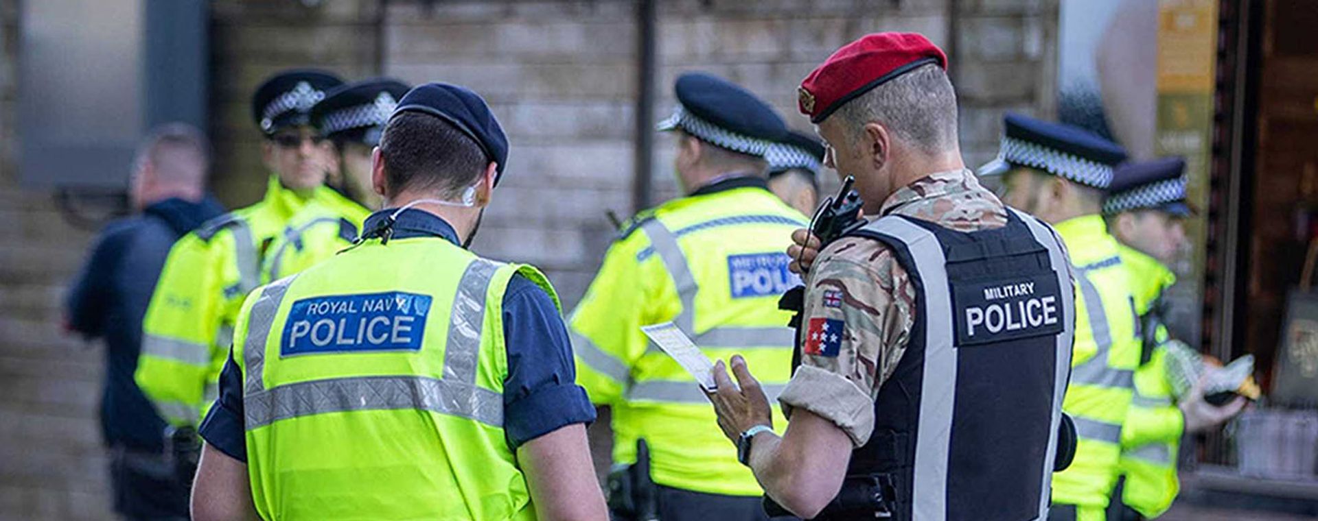 Group of uniformed police officers, including a military police member with red beret, gathered outdoors in high-visibility jackets.