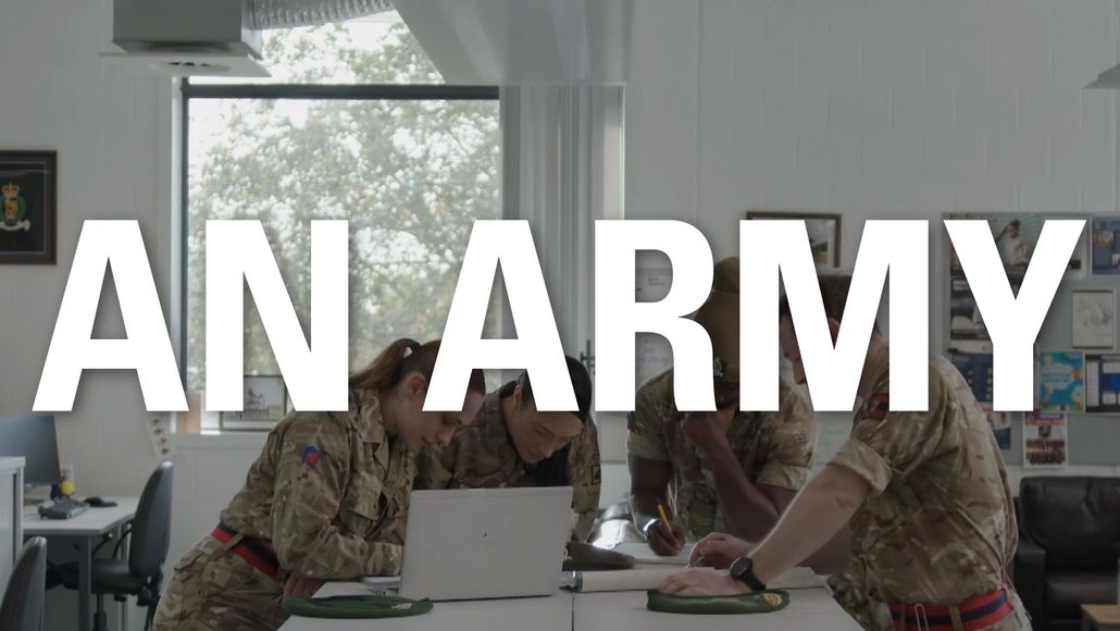 Group of male and female soldiers in an office gathered around a table and computer