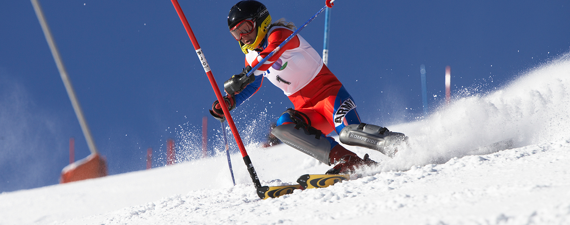 A skier in red and white gear navigates a slalom course on a snowy slope under a clear blue sky.