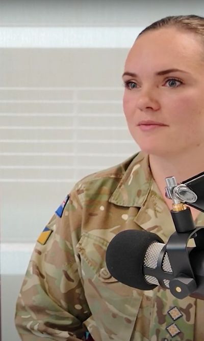 A person in military uniform speaks into a microphone. A smartphone screen displays "Prospects Future You" on a pink background.
