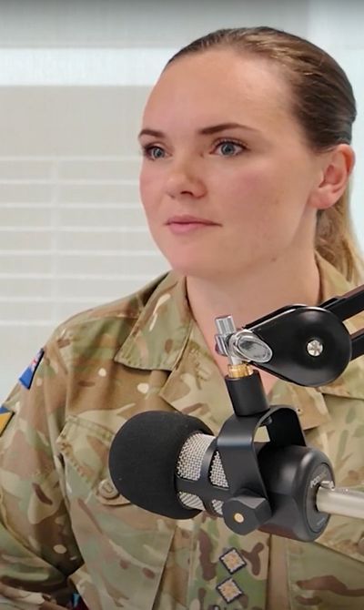 A person in military uniform speaks into a microphone. A smartphone screen displays "Prospects Future You" on a pink background.