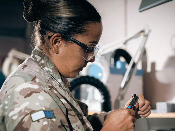 Female soldier working on wires with safety goggles on
