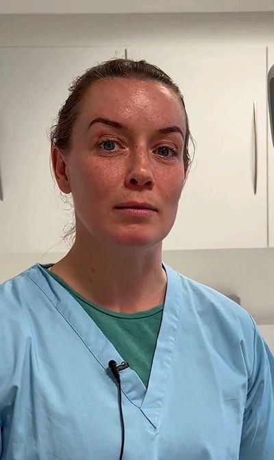 A woman in blue scrubs stands in a dental office, with cabinets and dental equipment in the background.