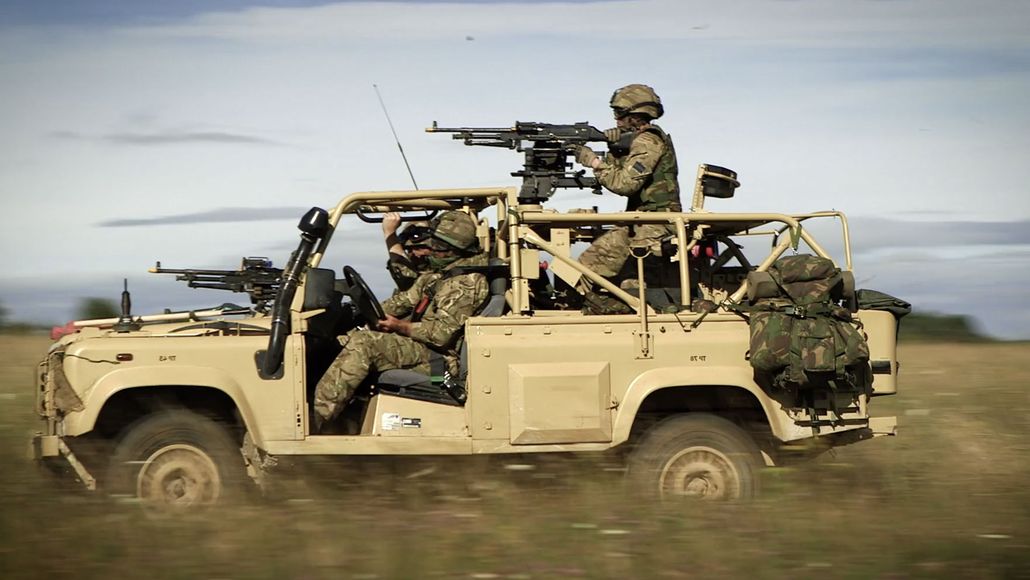 Soldiers driving through a field on a vehicle with mounted guns