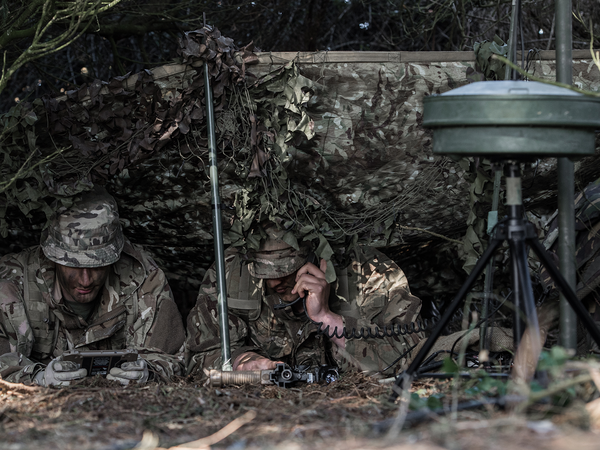 Soldiers on ground in camouflage using signal equipment