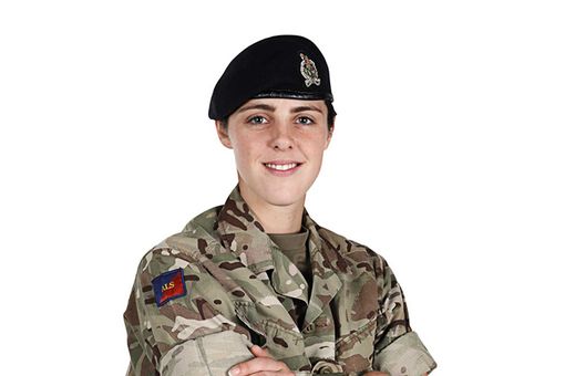 Person in military uniform with a black beret, smiling, arms crossed, against a white background.