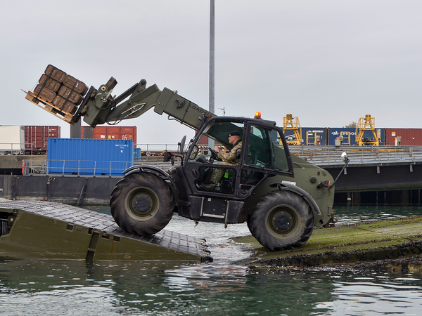 Port Operator transporting cargo onto a vessel with a mechanical arm vehicle
