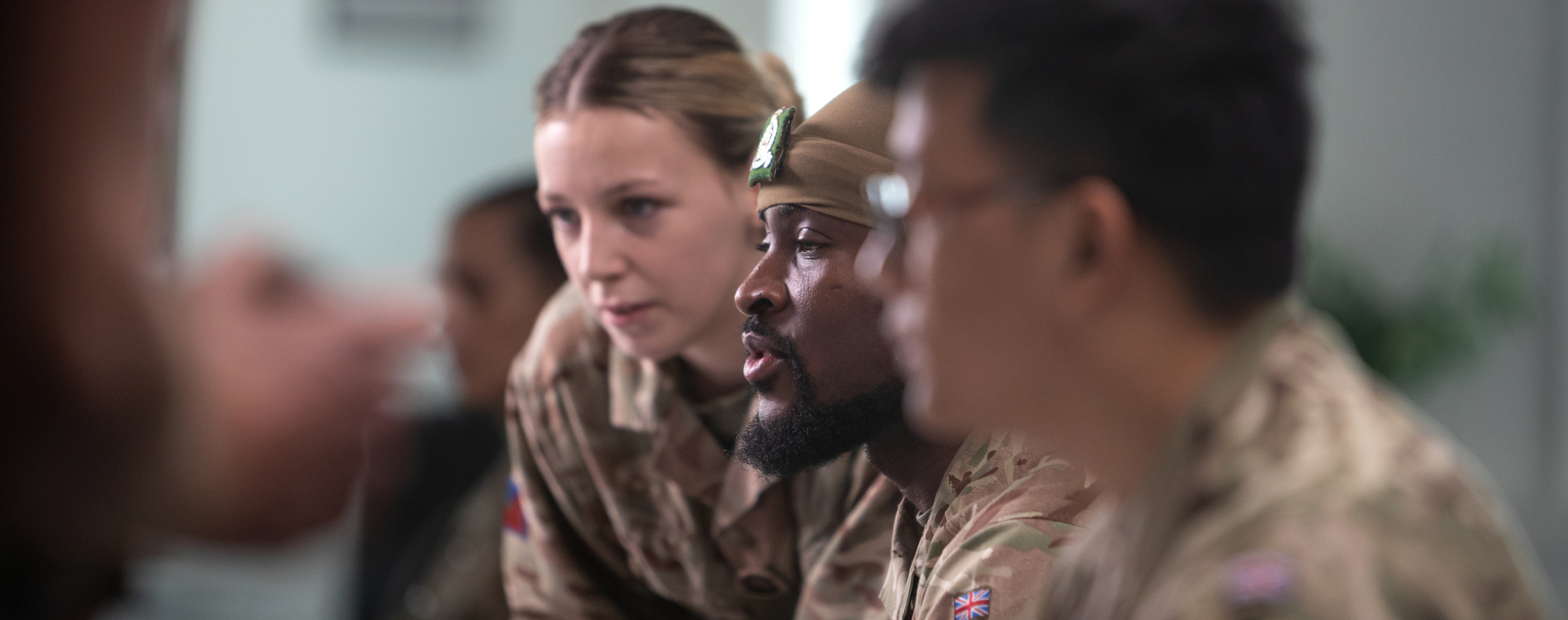 Military personnel in uniform attentively listen during a meeting in a bright room.
