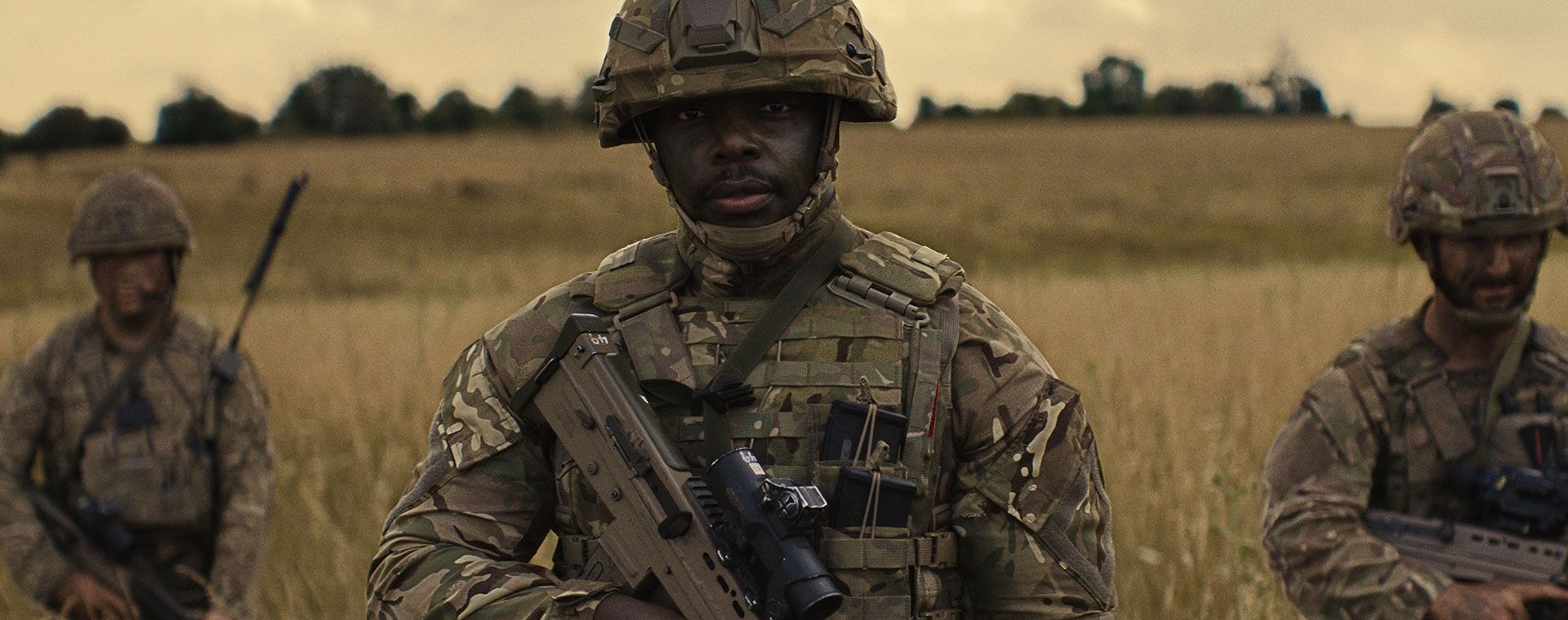 Soldiers in a field with guns looking directly at camera