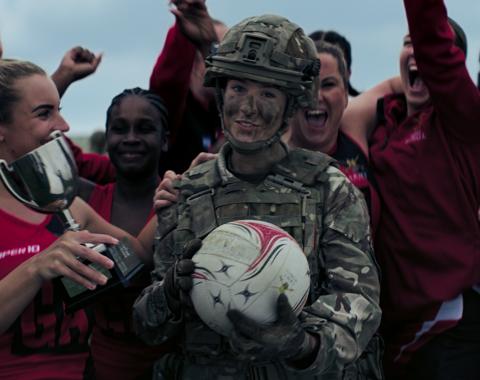 Female soldier on camo gear surrounded by sports team
