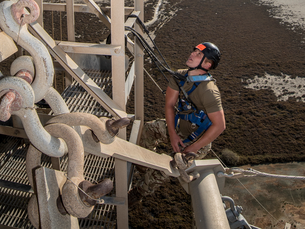Soldier in climbing harness up a structure looking up