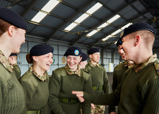 A group of uniformed military personnel in a hangar, smiling and interacting with each other.