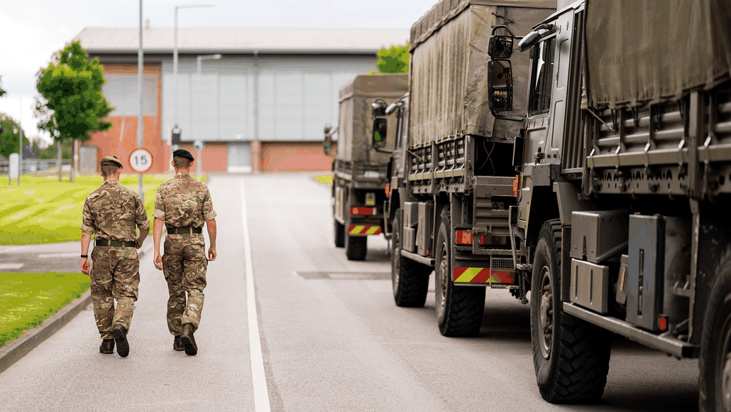 two soldiers walking away next to a number of Army lorries on camp