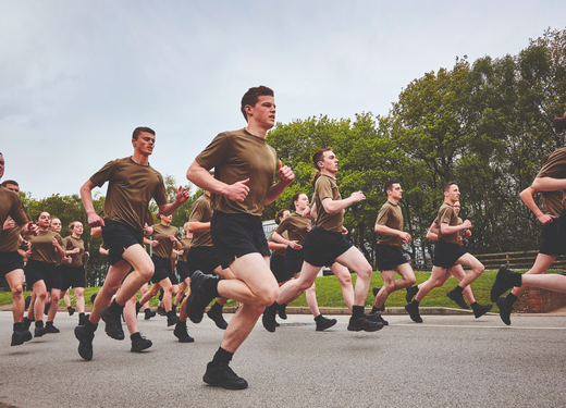 A group of people in matching brown shirts and black shorts running together on a paved path, with trees and greenery in the background.