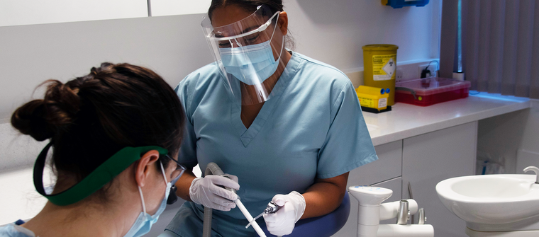 female dental nurse in blue scrubs assisting a dentist in treatment room