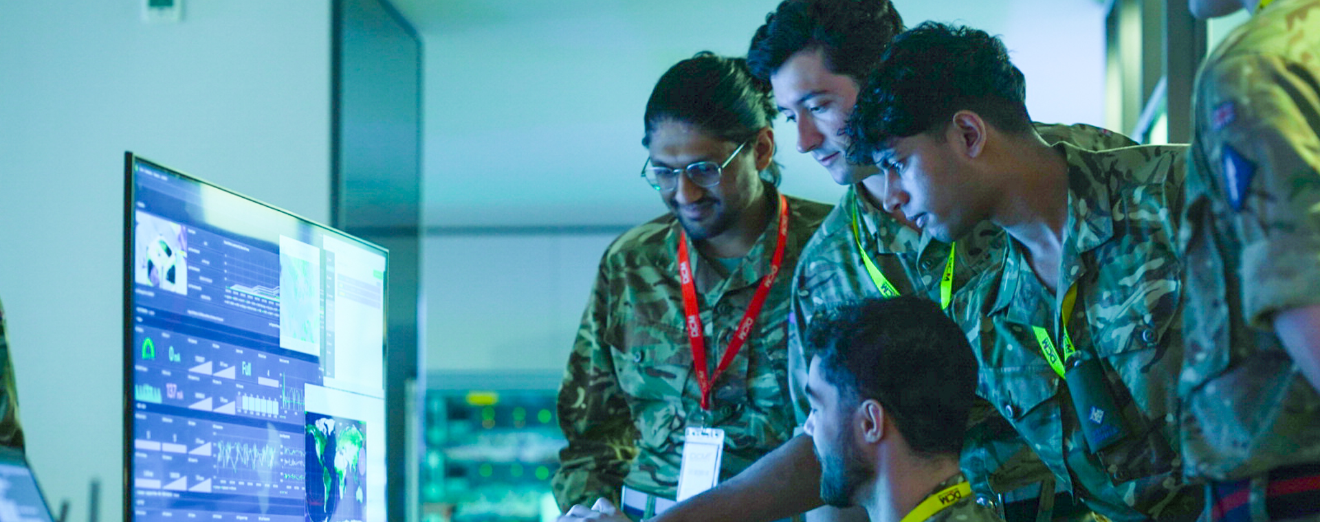 Soldiers in camouflage uniforms analyze data on large screens in a command center, discussing strategy with focused expressions.