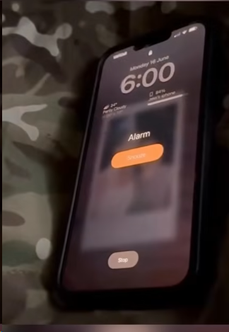 Smartphone displaying a 6:00 AM alarm on a camouflage-patterned surface, with options to snooze or stop.