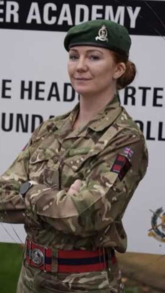 Female soldier standing with her arms crossed in front of a sign