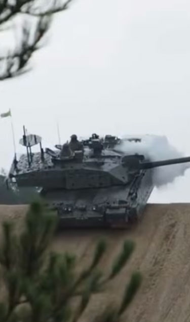 A tank advancing on a dirt road, partially obscured by smoke, with a tree in the foreground.