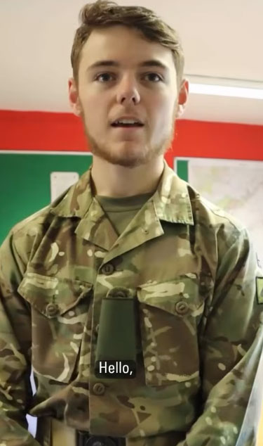 Young man in military uniform stands indoors, facing the camera, with a map and red wall in the background. Subtitled "Hello".