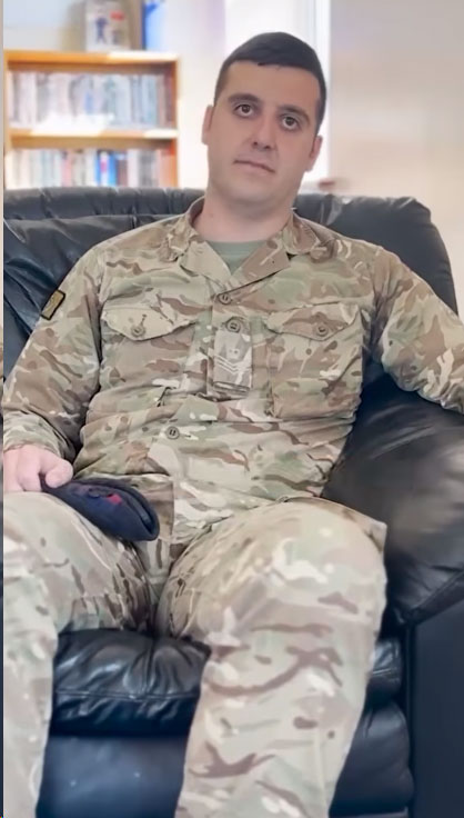 Soldier sitting in an arm chair, holding his beret, looking to camera